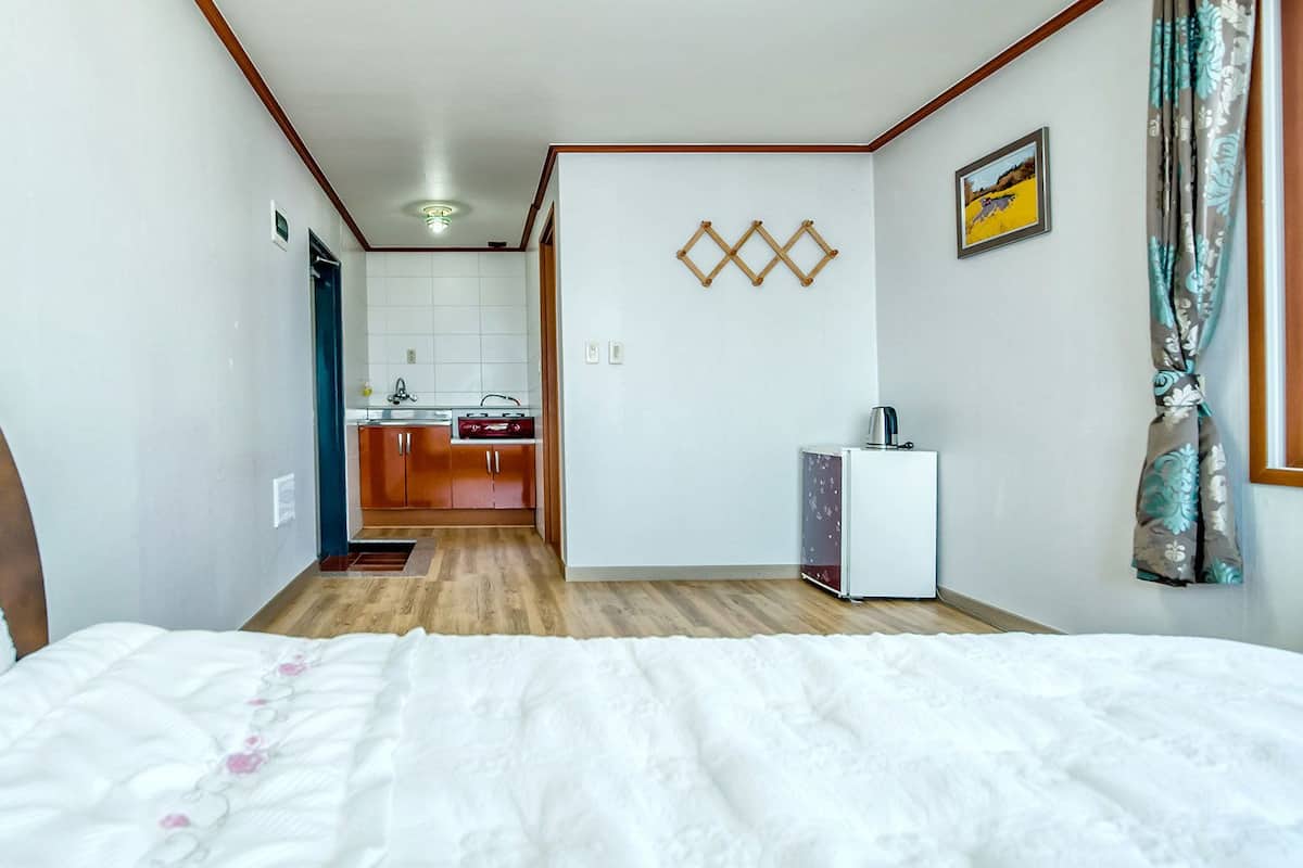 A hotel room with a bed, a small kitchenette, and a bathroom visible through an open door.