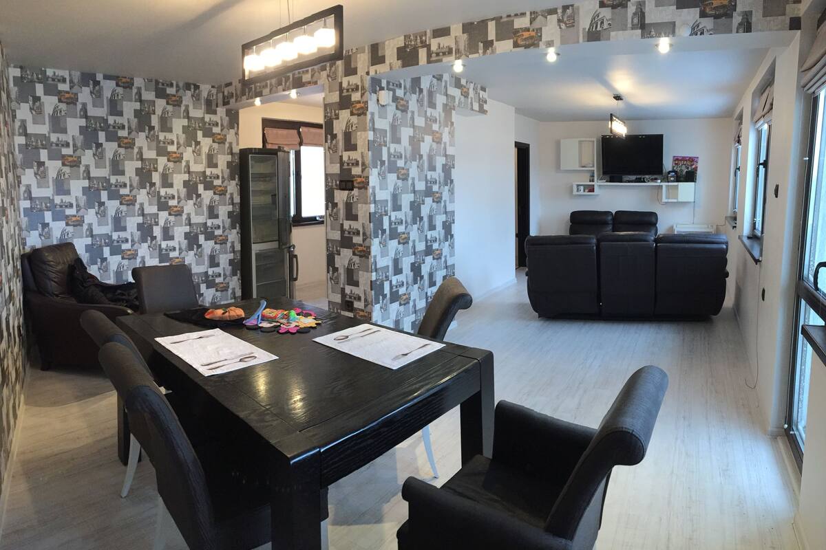 A modern living room with a dining area, featuring a black dining table, black chairs, and a black sofa.