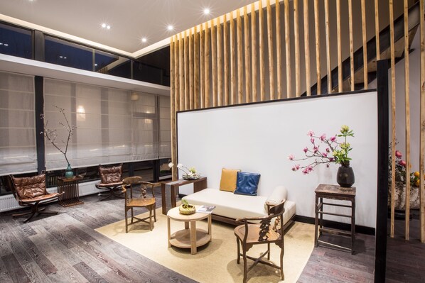 Una sala de estar moderna con sofá, sillas y una mesa de centro. Se observa una pared de listones de madera y un ventanal grande.