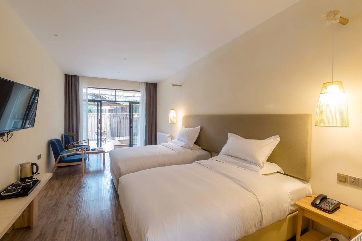 Habitación de hotel con dos camas, un televisor, un escritorio con hervidor y vistas al exterior.
