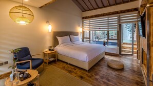 A bedroom with a large bed, a chair, a bedside table, a lamp, and a window with blinds. - Sukham Advesa Emei (Leshan)