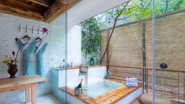 A modern spa room with a wooden bench, a glass-enclosed hot tub, and a bamboo wall. - Sukham Advesa Emei (Leshan)