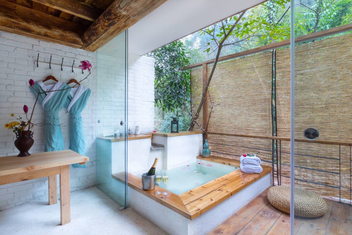 Un spa moderno con un banco de madera, una bañera de hidromasaje con recinto de vidrio y una pared de bambú.