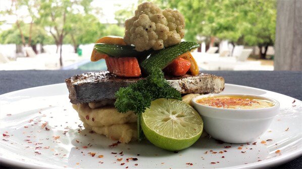 A plate of food with a fish fillet, vegetables, and a lime wedge.