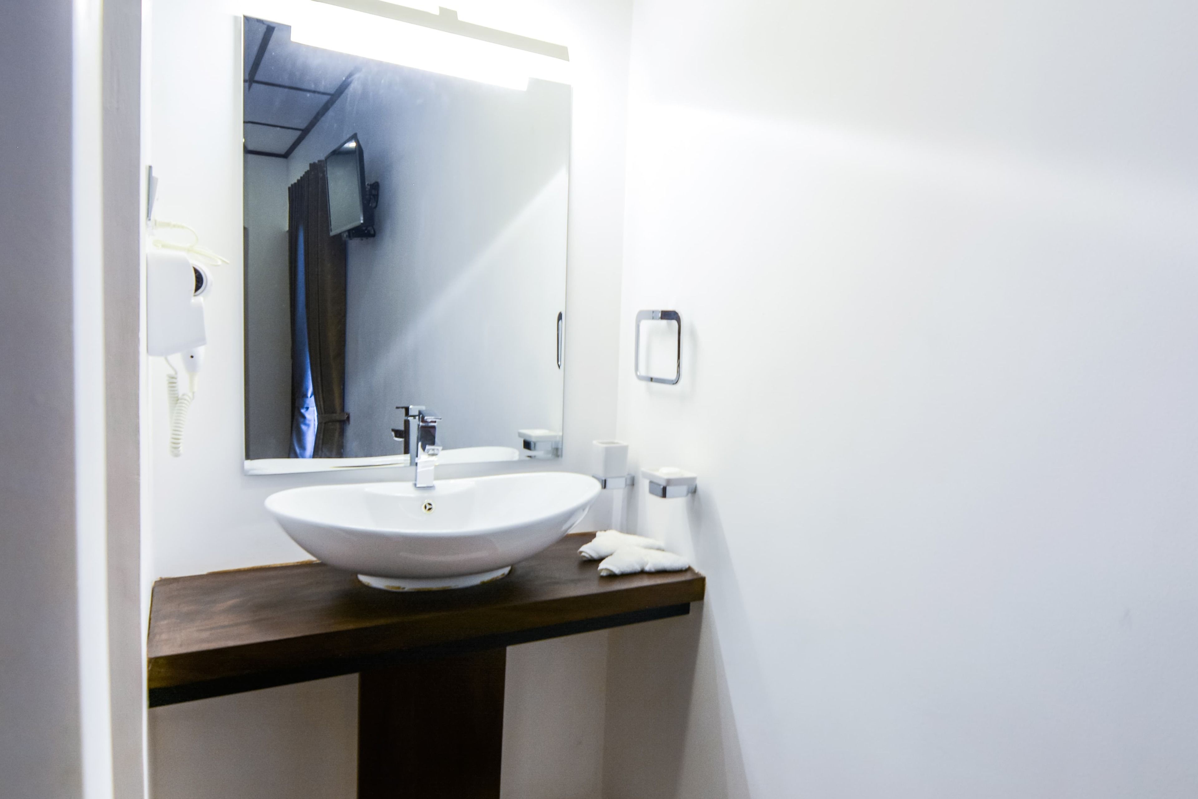 Un baño con un lavabo blanco, un espejo, un secador de pelo y una toalla sobre el mostrador.