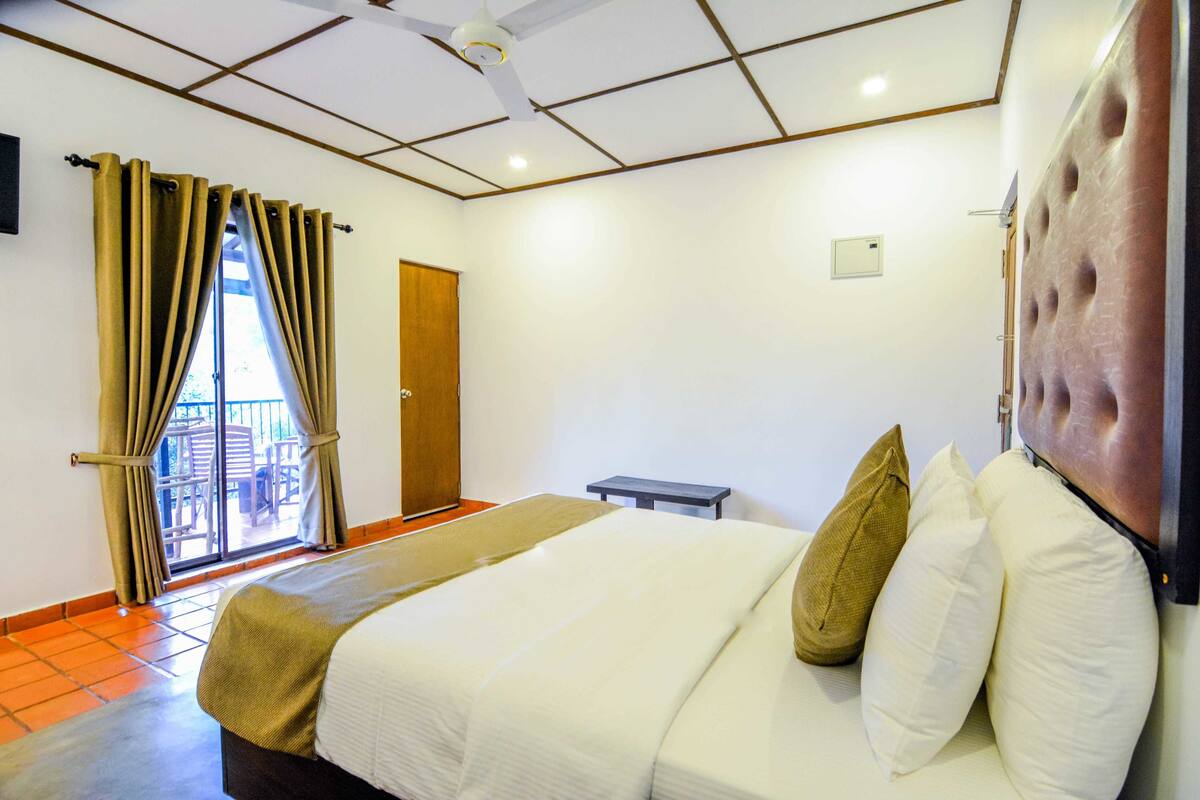 Une chambre d’hôtel avec un lit, des rideaux, un ventilateur de plafond et une vue sur l’extérieur.