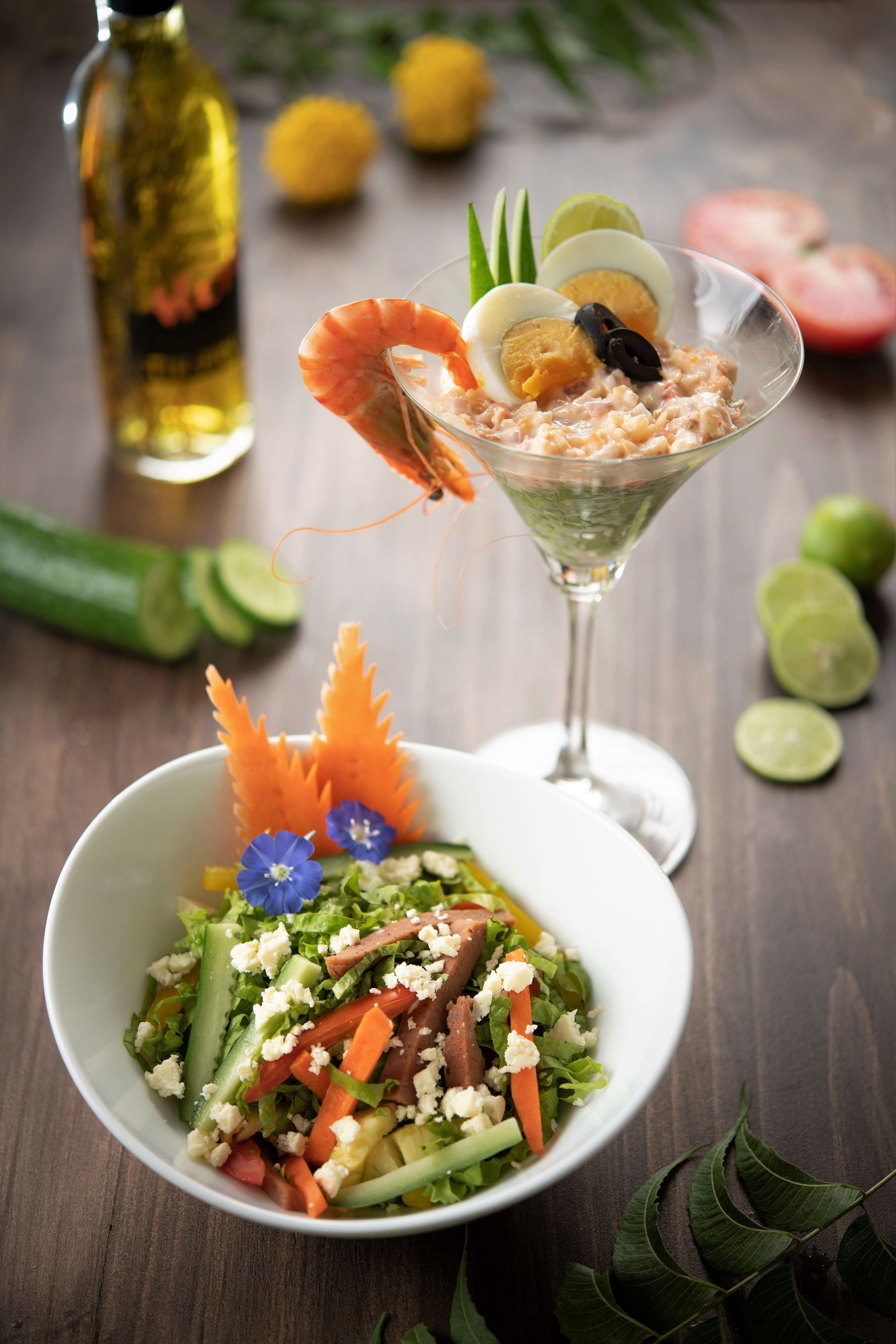 A martini glass with shrimp, egg, and olives, and a bowl of salad with feta cheese and vegetables.