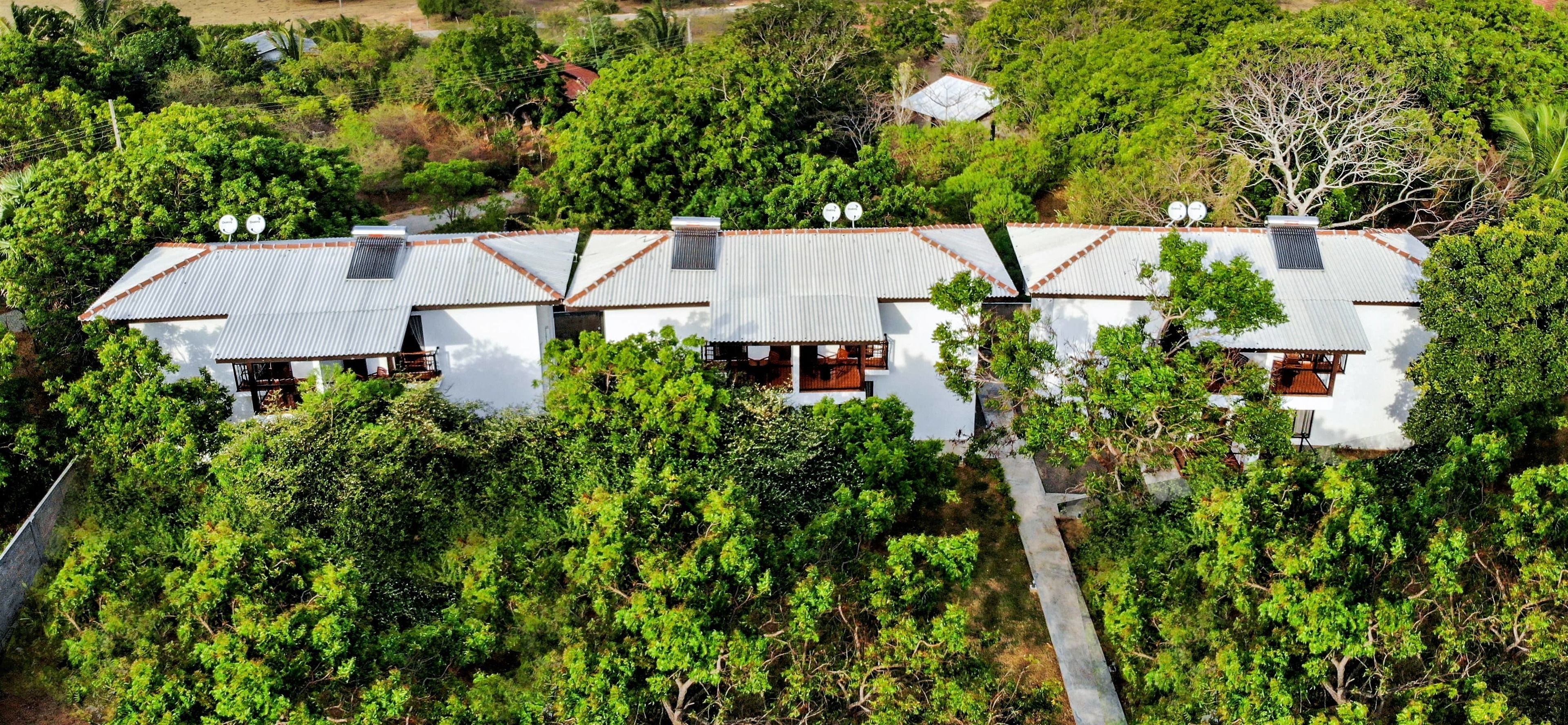 A row of white buildings with metal roofs, surrounded by dense greenery.