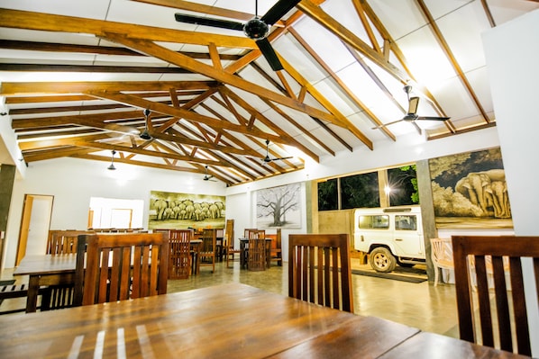 A spacious dining area with wooden beams and ceiling fans, a white SUV parked by the window, and artwork on the walls.