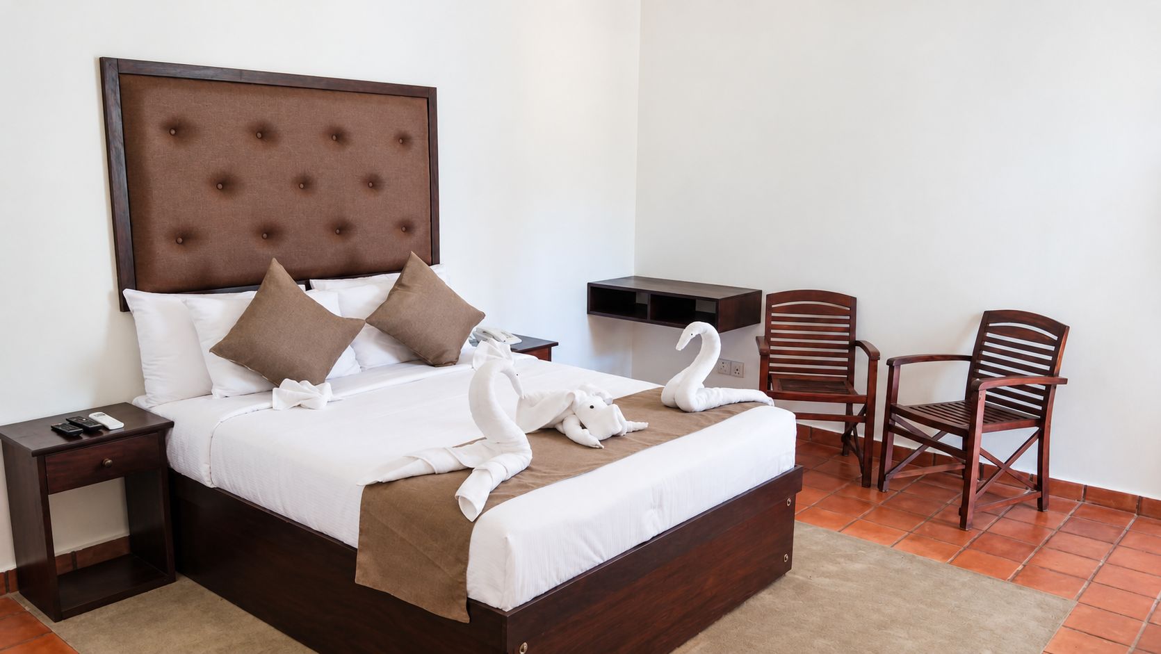 A hotel room with a large bed, two wooden nightstands, a wooden chair, and a desk with a chair.