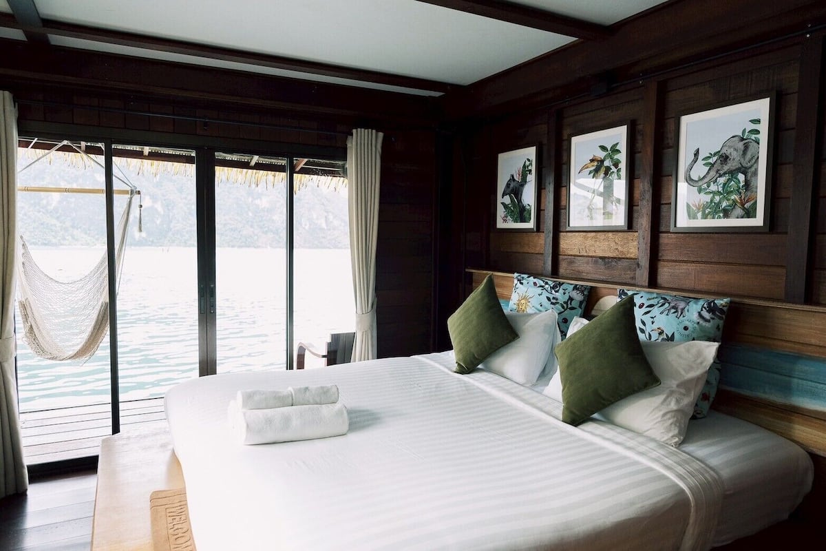 A bedroom with a large bed, a hammock, and a view of the water.