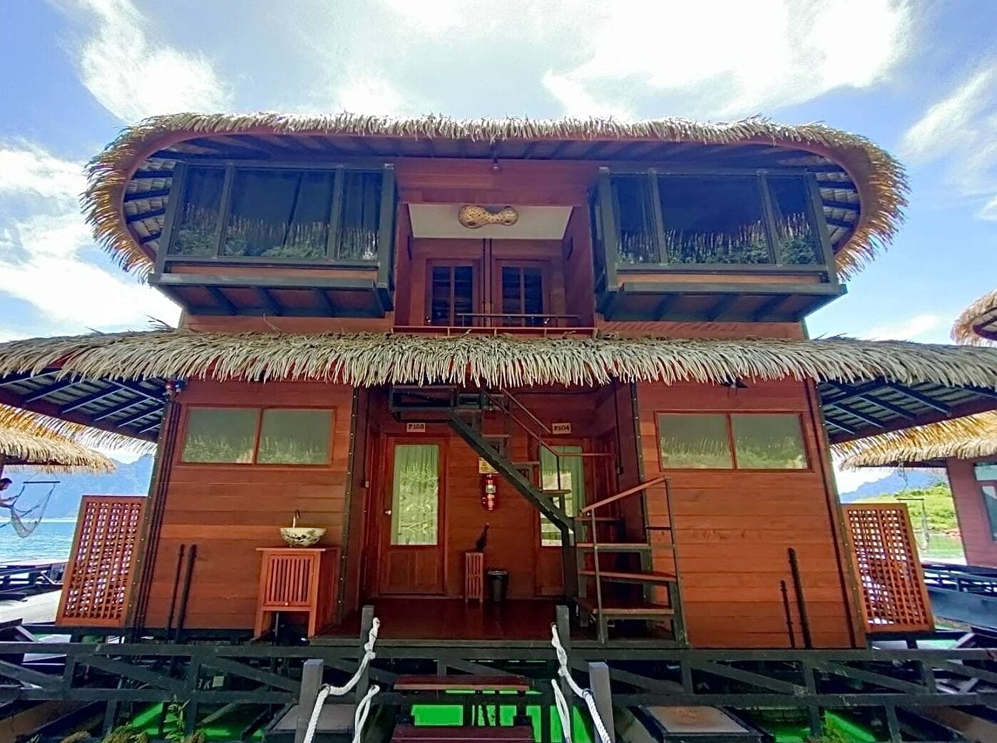 A two-story wooden house with a thatched roof, a staircase leading to the upper floor, and a view of the sea.