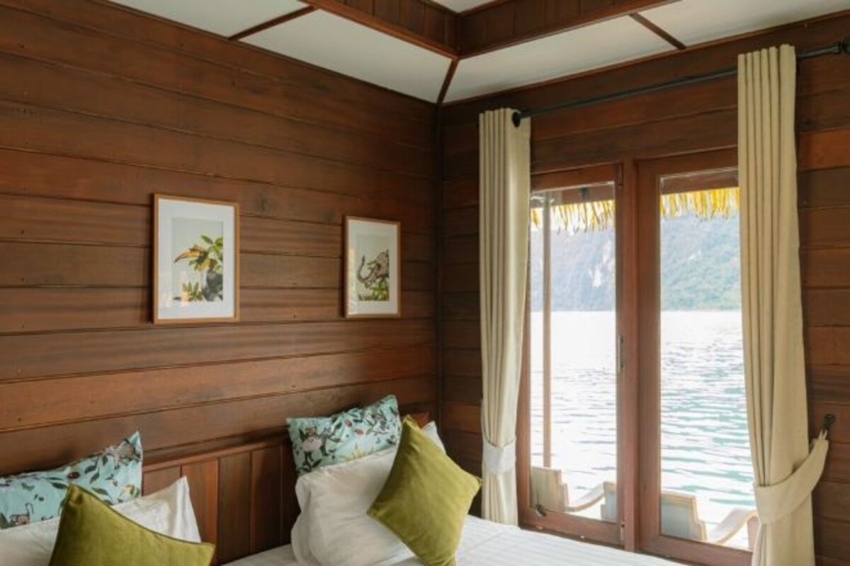 A wooden cabin room with a bed, two framed pictures, and a window overlooking water.