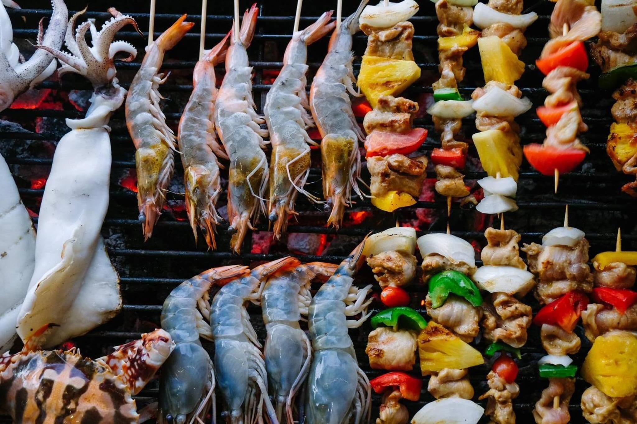 Diversas brochetas de mariscos y alimentos a la parrilla sobre una plancha.