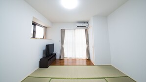 A room with a television on a stand, a window, and an air conditioning unit. - Maruka Ishigakijima (Ishigaki)