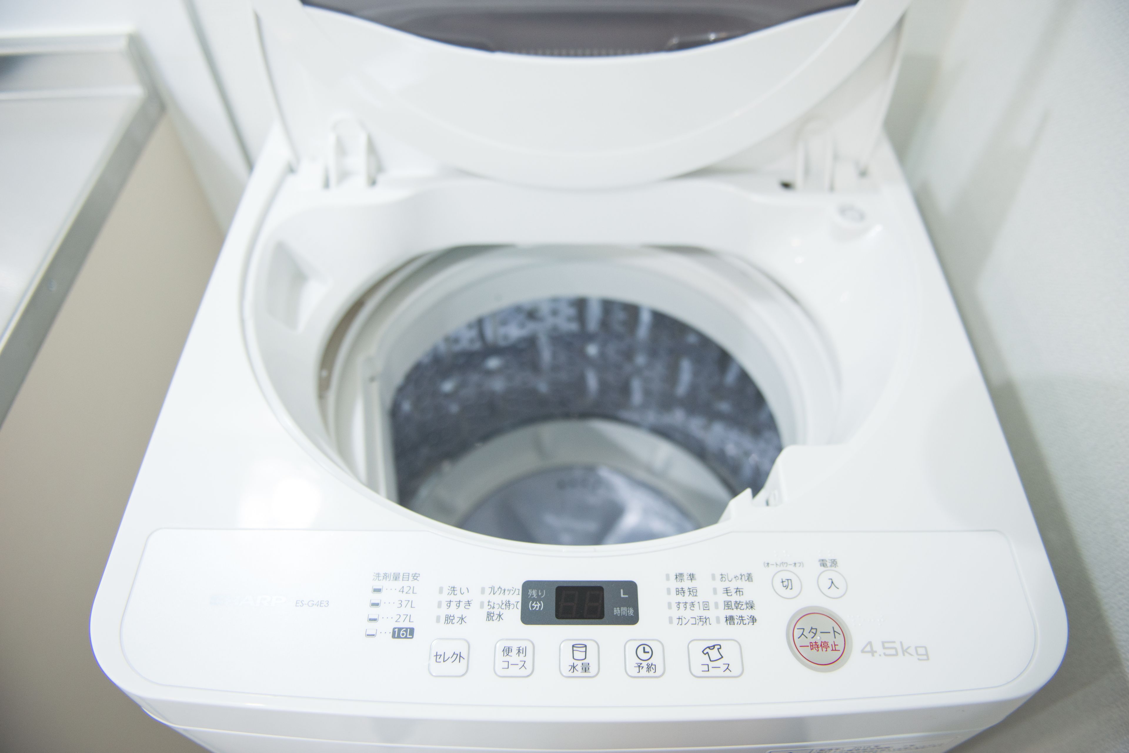 A front view of a modern, white, front-loading washing machine with a digital display and multiple control buttons.