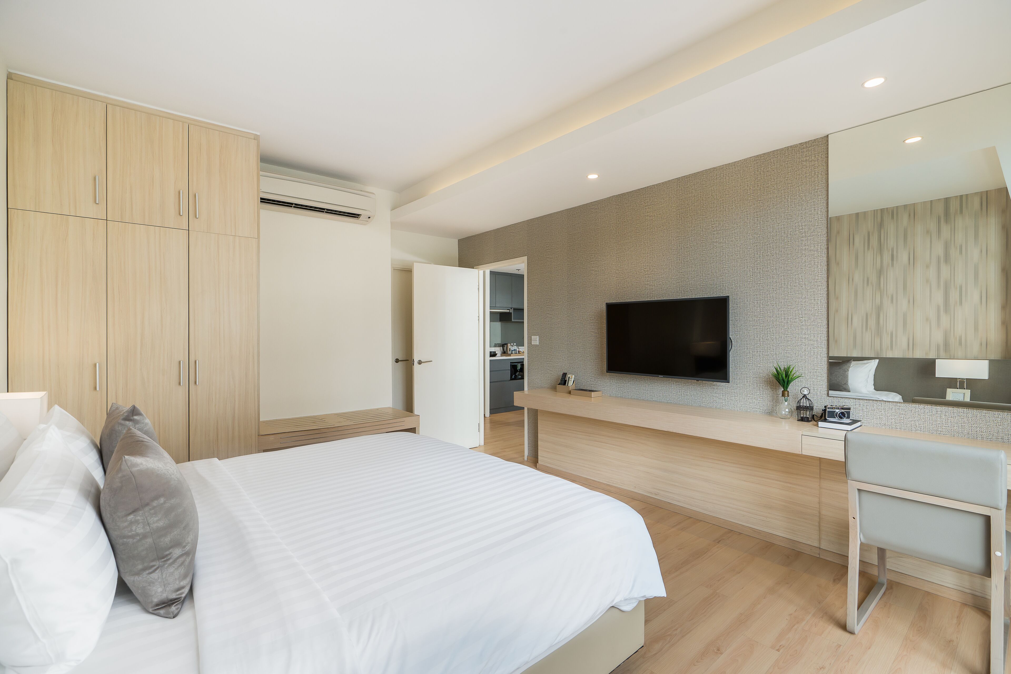 A modern hotel room with a large bed, a TV mounted on the wall, a desk, and a seating area.