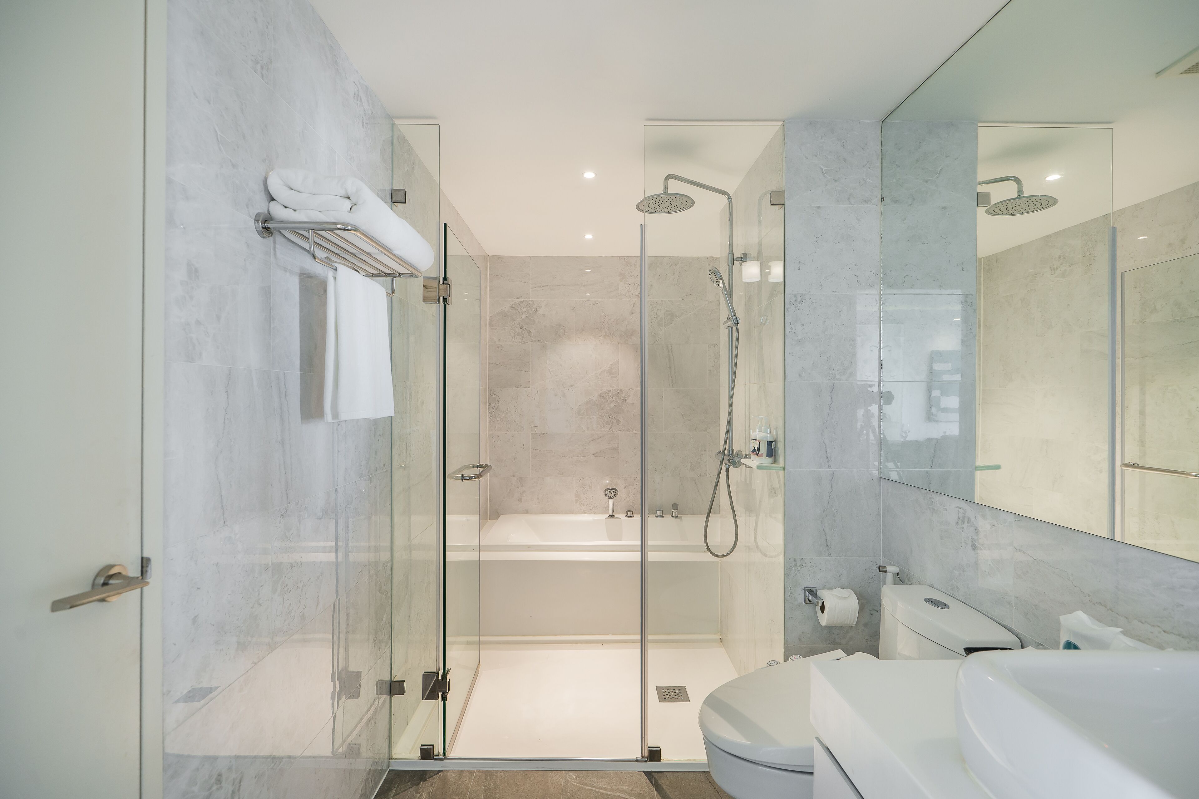 A modern bathroom with a glass-enclosed shower, a separate bathtub, and a vanity with a large mirror.