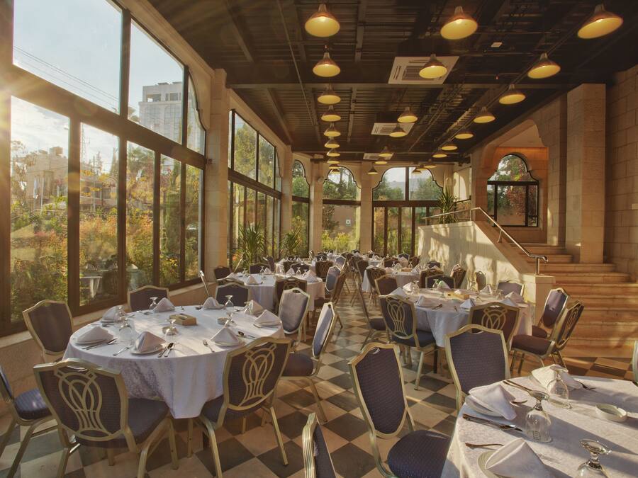 Un comedor con mesas y sillas redondas, ventanas amplias y una escalera.