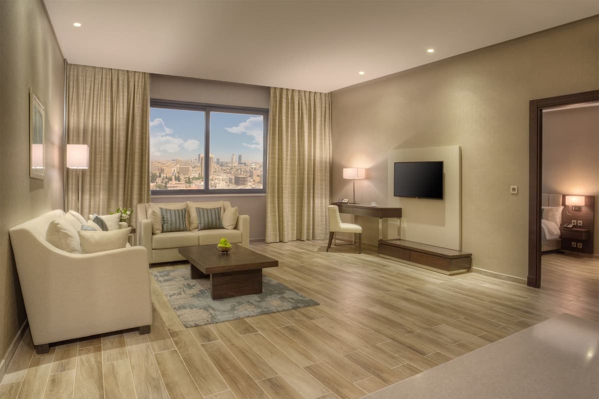 Una habitación de hotel moderna con sofá, una mesa de centro, televisor y escritorio.
