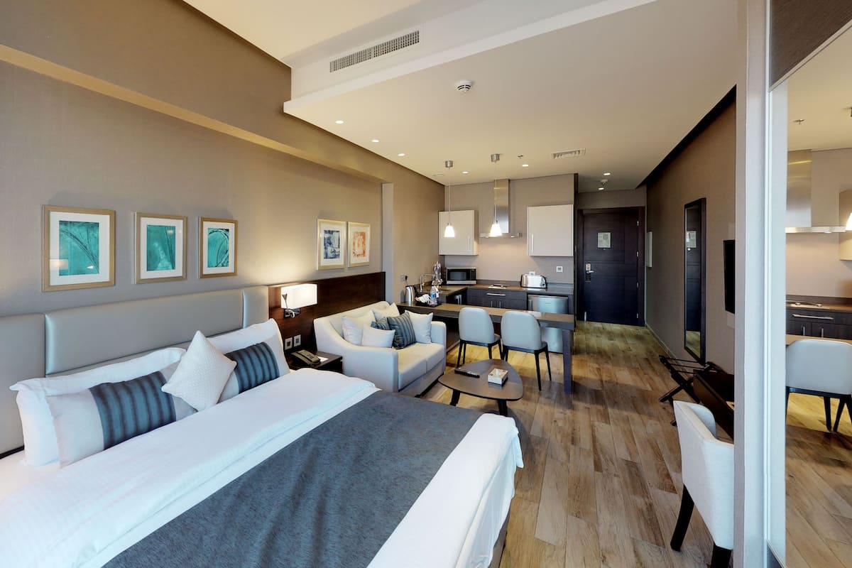 Una habitación de hotel con una cama grande, dos mesitas de noche, un escritorio, un sofá y una kitchenette.
