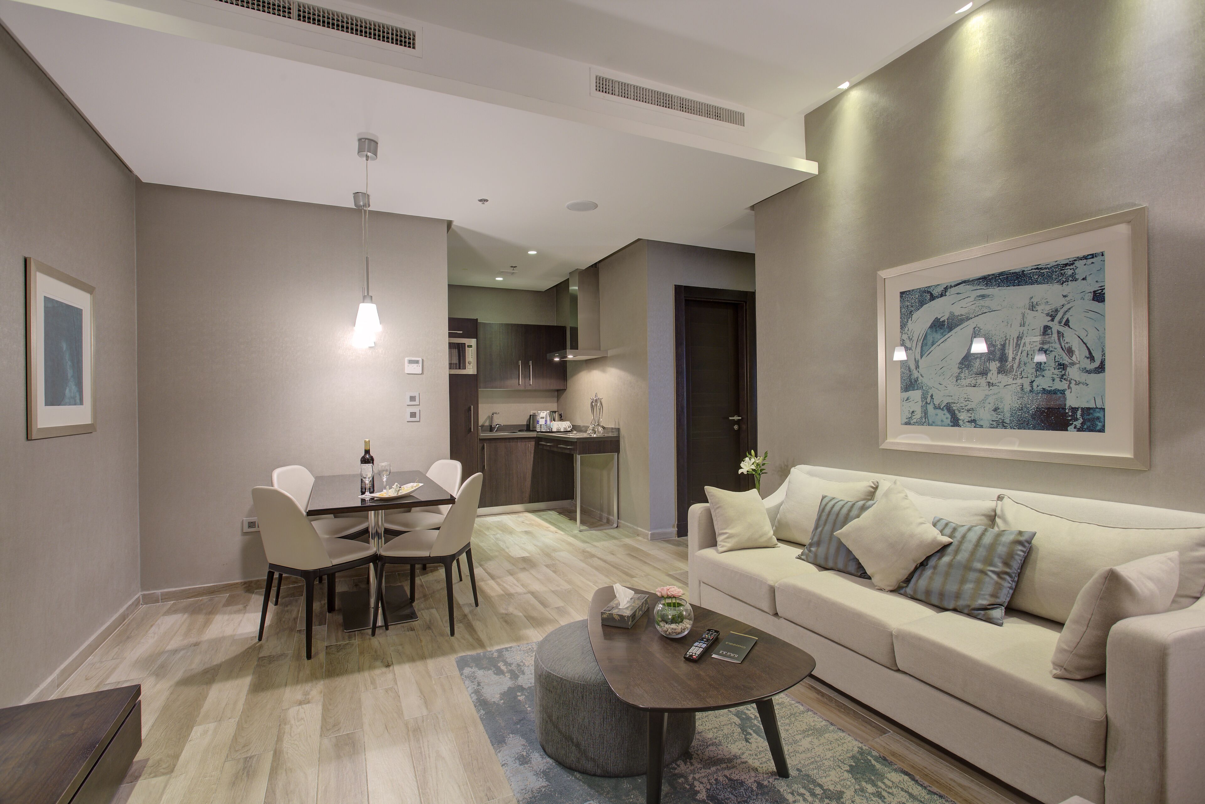 A modern living room with a dining area, a kitchen in the background, and a large framed artwork on the wall.