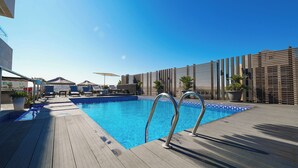 Un área de piscina con cubierta de madera, sillas de descanso y sombrillas.