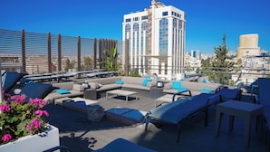 Un salón en la azotea con asientos al aire libre, una mesa de centro y vistas a edificios de la ciudad.