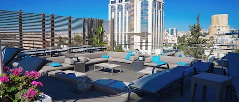 A rooftop lounge with outdoor seating, a coffee table, and a view of city buildings.