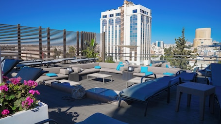 A rooftop lounge with outdoor seating, a coffee table, and a view of city buildings.
