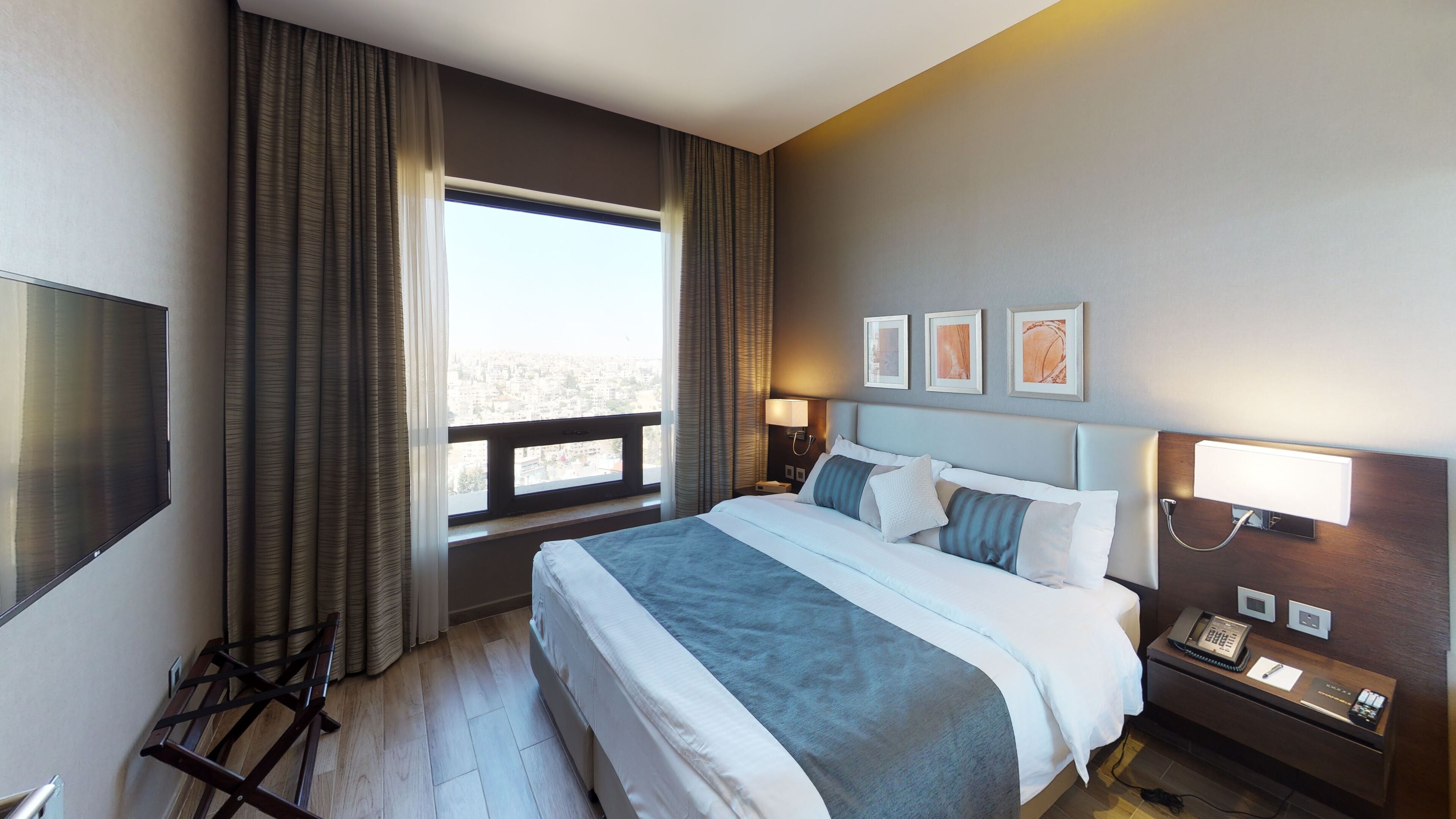 Una habitación de hotel con una cama grande, un escritorio con teléfono, un televisor y una ventana con cortinas.