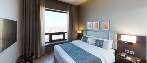 Una habitación de hotel con una cama grande, un escritorio con teléfono, un televisor y una ventana con cortinas.