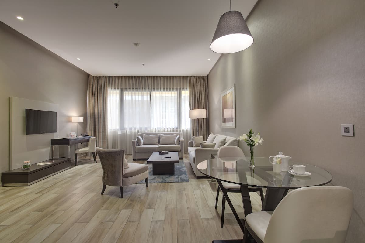 Una sala de estar moderna con un conjunto de sofá, una mesa de centro, una mesa de comedor de vidrio y un televisor montado en la pared.