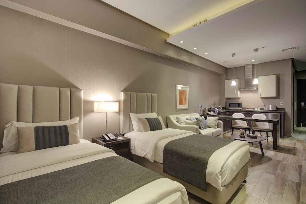 Habitación de hotel con dos camas, un escritorio, una silla, una mesita y una kitchenette.