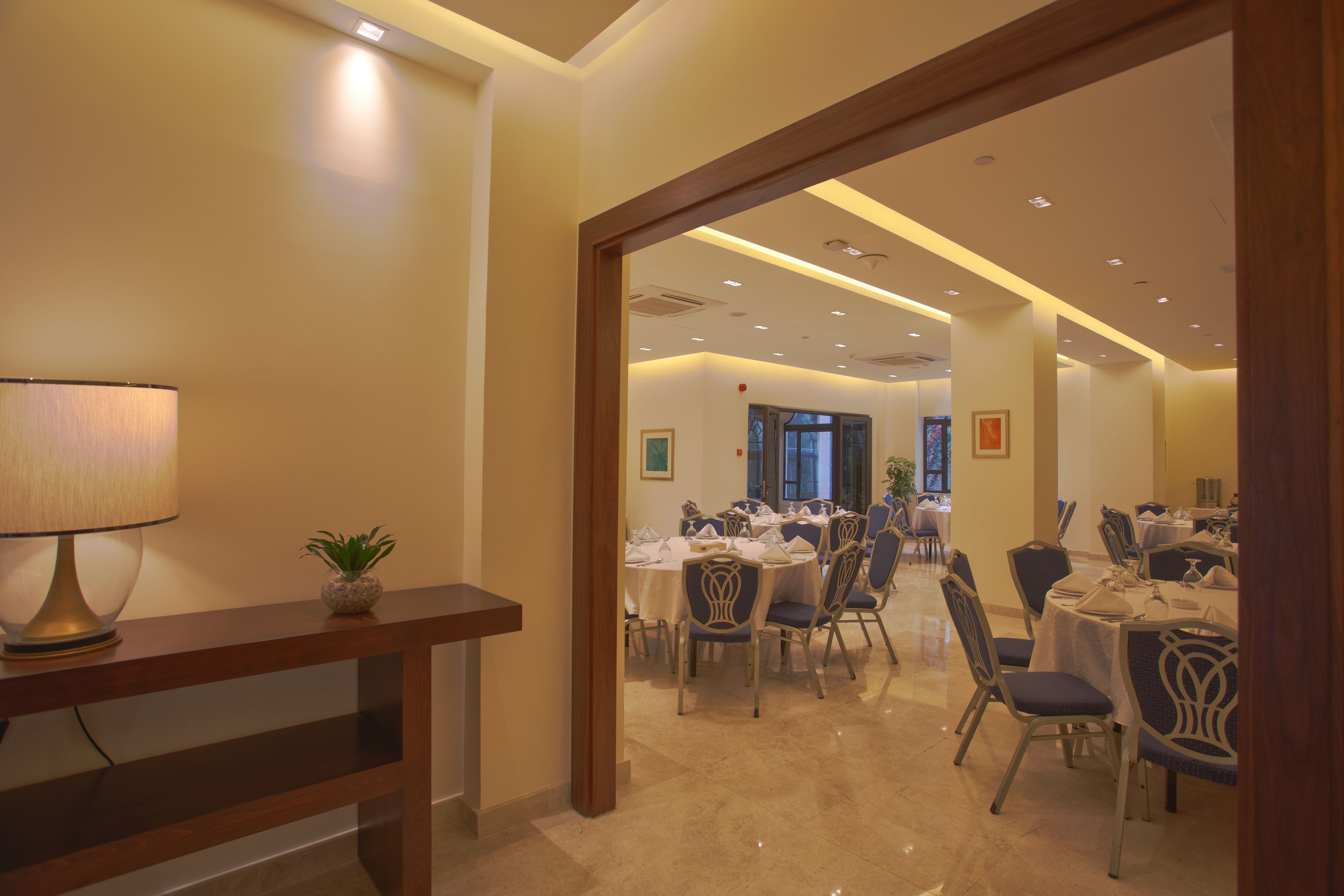 Un comedor de hotel con varias mesas y sillas, una lámpara y una planta en maceta.