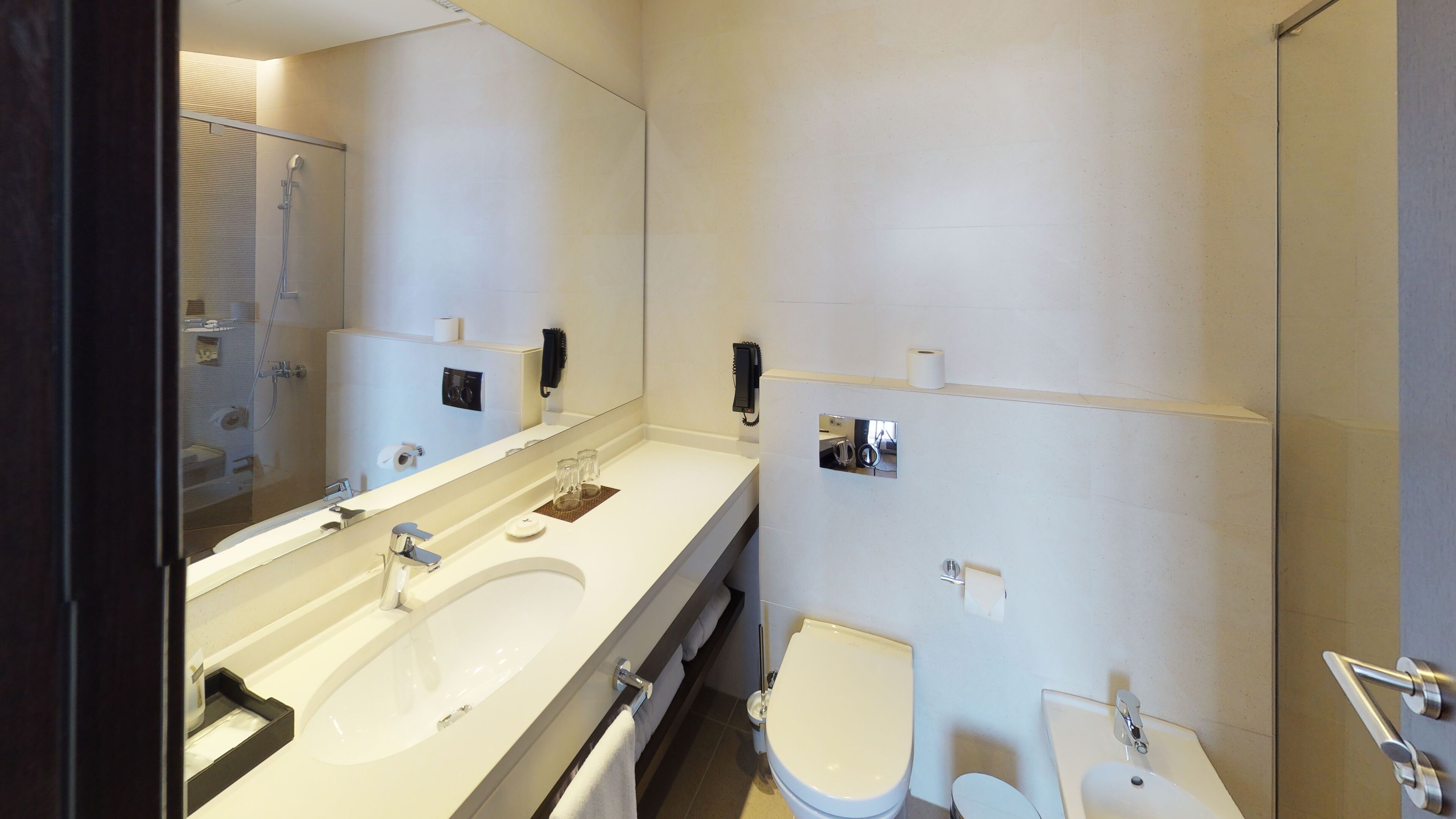 A modern bathroom with a large mirror, two sinks, a toilet, and a shower.