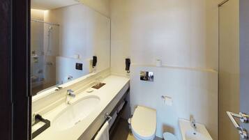 A modern bathroom with a large mirror, two sinks, a toilet, and a shower.
