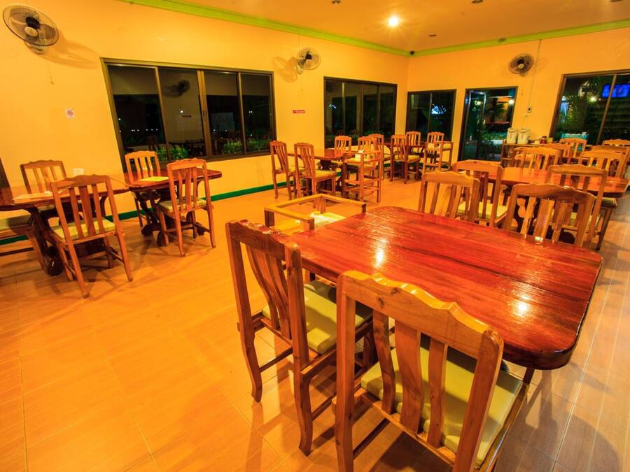 A spacious dining area with multiple wooden tables and chairs, large windows, and ceiling fans.