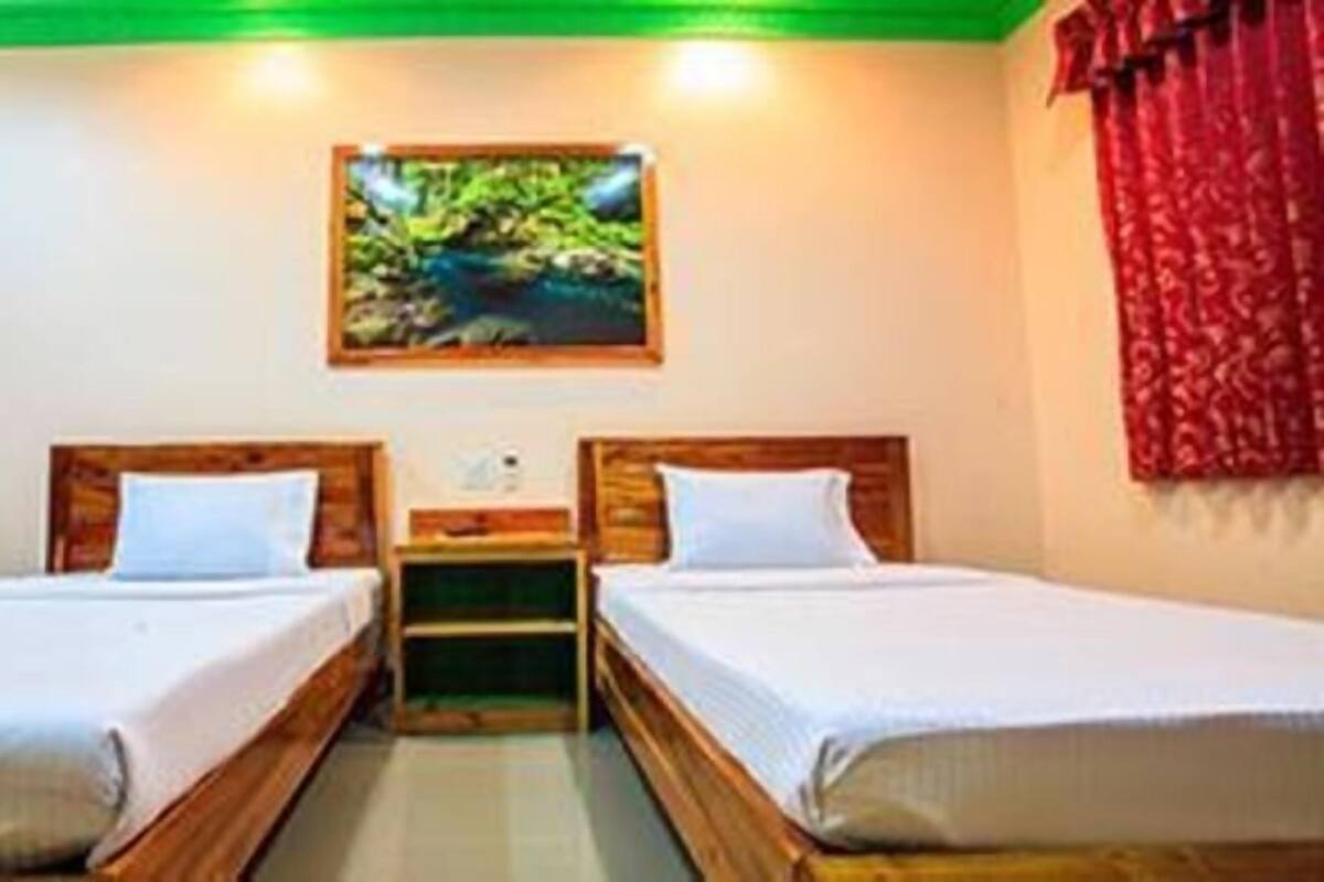 Ein Zimmer mit zwei hölzernen Betten, einem Nachttisch dazwischen, einer grünen Decke und einem Bild an der Wand.