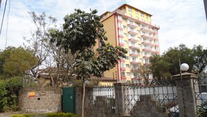 A multi-story residential building with a yellow and red facade, a gated entrance, and a tree in the foreground. - Tawala Homes (Nairobi)
