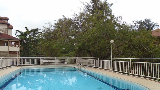 A rectangular swimming pool with a white metal fence and a tiled deck surrounding it. - Tawala Homes (Nairobi)
