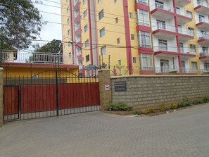 Un edificio de apartamentos de varios pisos con fachada roja y amarilla, entrada protegida por un portón y un letrero que indica que son apartamentos con servicios.