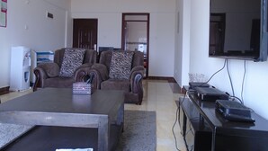 A living room with a sofa set, a coffee table, a flat-screen TV, and a small table with electronic devices. - Tawala Homes (Nairobi)