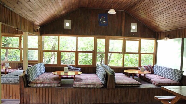 A cabin with a sloped ceiling, wooden walls, and large windows offering views of greenery. There are multiple seating areas with cushions and tables. - Camlik Pansiyon - Adults Only (16+) (Kumluca)
