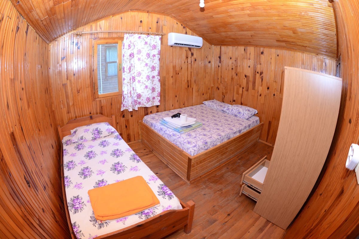Ein Schlafzimmer einer Holzhütte mit zwei Betten, einem Fenster mit Blumenvorhang und einer Klimaanlage.