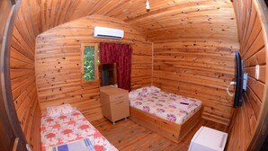 A wooden cabin room with two beds, a small dresser, an air conditioning unit, and a heater. - Camlik Pansiyon - Adults Only (16+) (Kumluca)