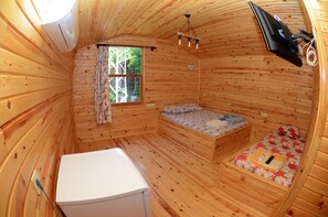 A compact wooden cabin room with a bed, a small table, a window with curtains, and a ceiling fan. - Camlik Pansiyon - Adults Only (16+) (Kumluca)