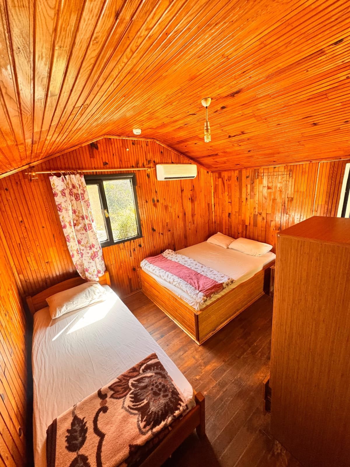 A wooden cabin room with a bed, a window, and an air conditioning unit.