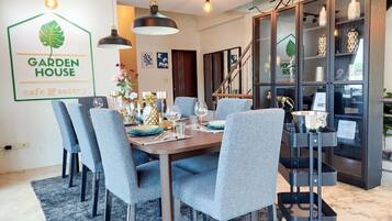 Zona pranzo con tavolo imbandito per sei persone, sedie grigie rivestite in tessuto, illuminazione a sospensione e una vetrina con oggetti decorativi.