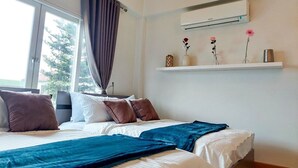 Una cama bien hecha con una manta azul, una ventana con cortinas y un aire acondicionado de pared.
